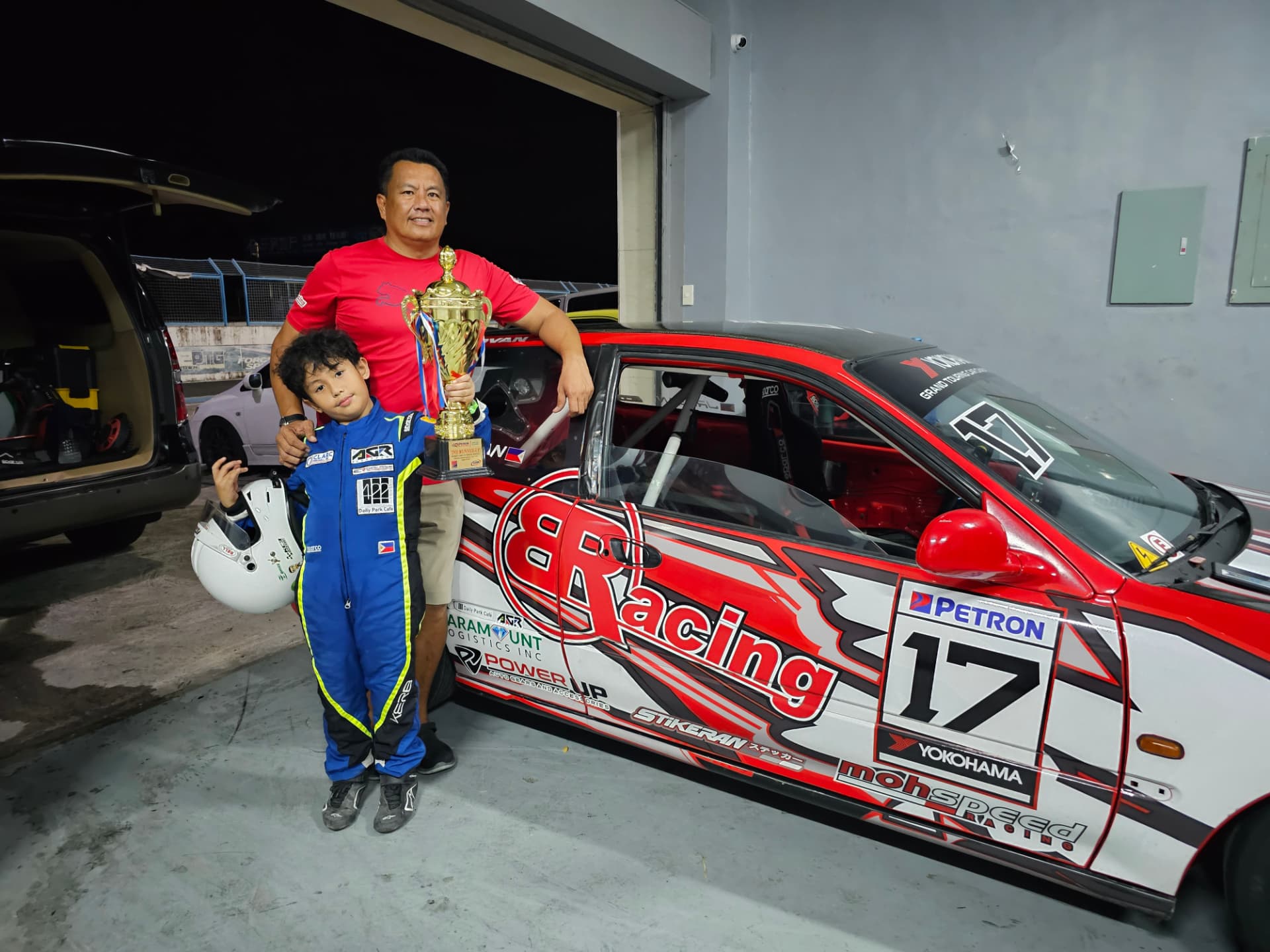 Antonio Racelis with a trophy beside his father and a race car
